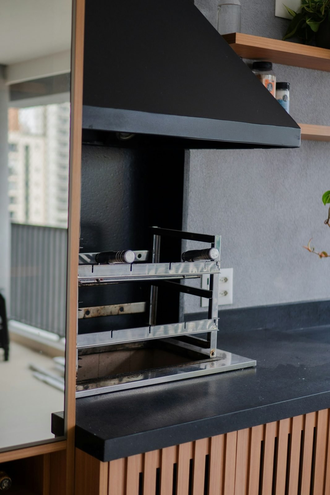 Built-in grill with black hood and dark granite countertop on an apartment balcony