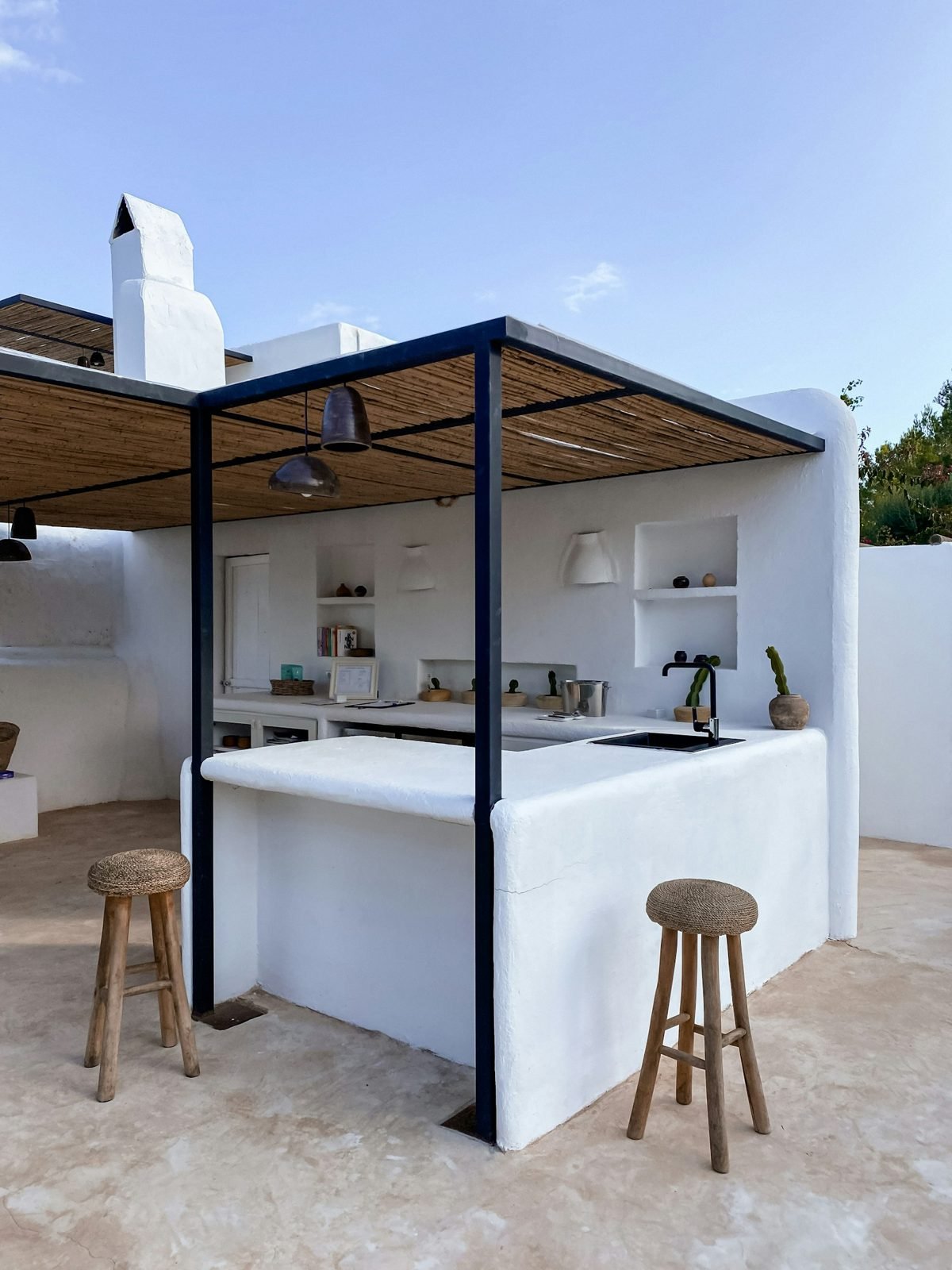 White masonry outdoor kitchen with pergola, counter and wooden stools