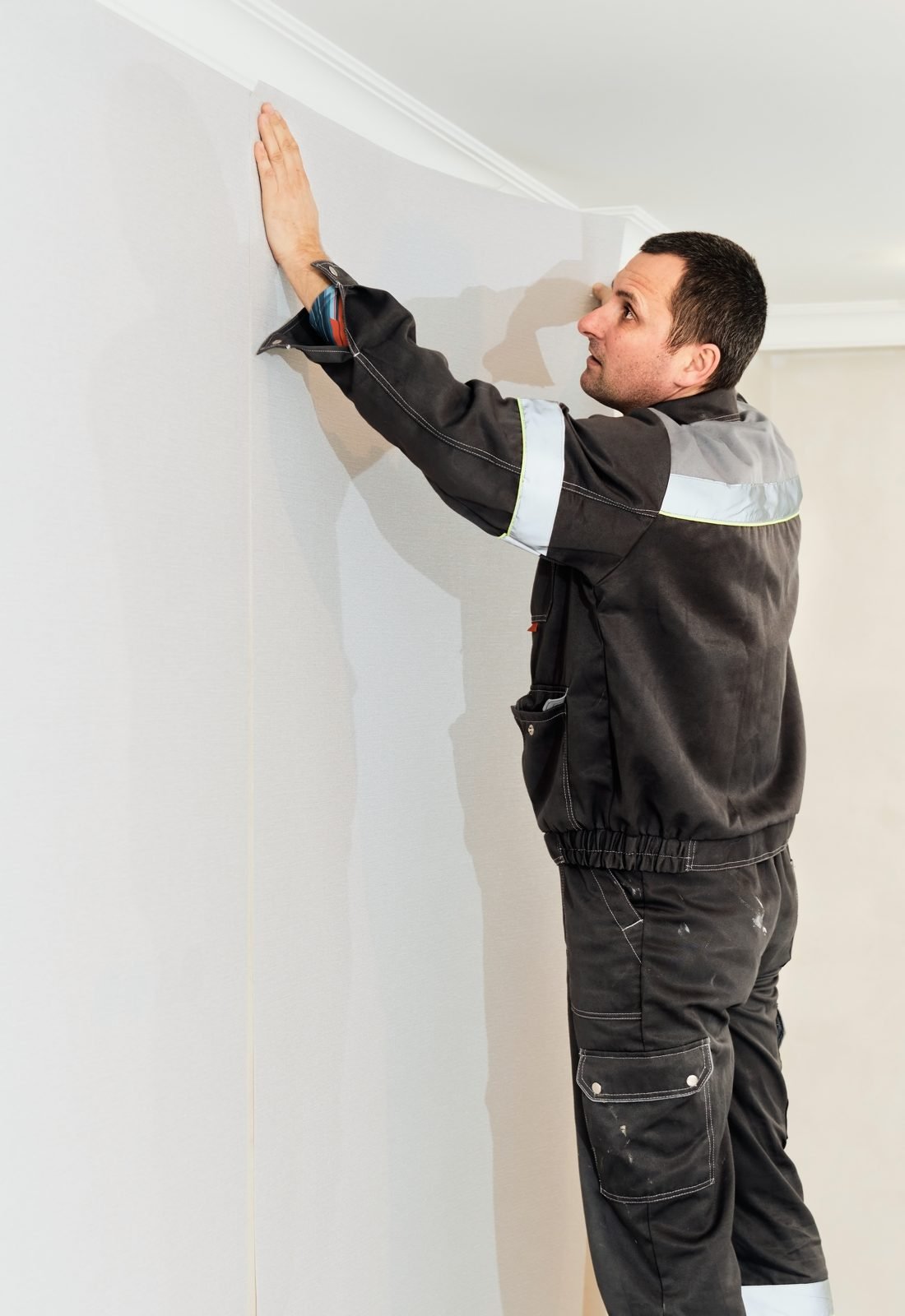 Person positioning a strip of light wallpaper at the top of a wall, right below the ceiling