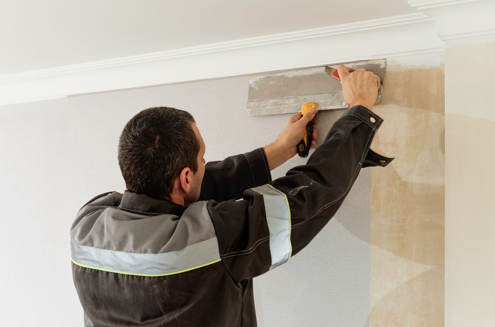 Trimming wallpaper along the ceiling molding with a wide metal knife and a utility knife