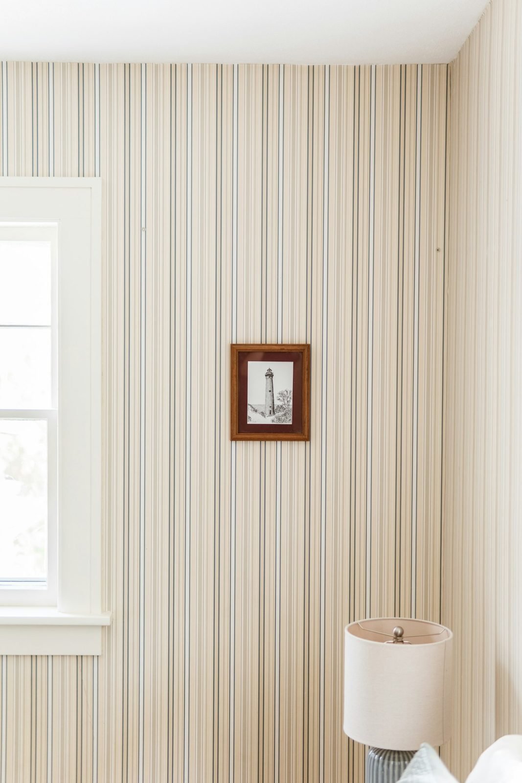 Wall covered in beige and blue striped wallpaper next to a white window and a small framed picture