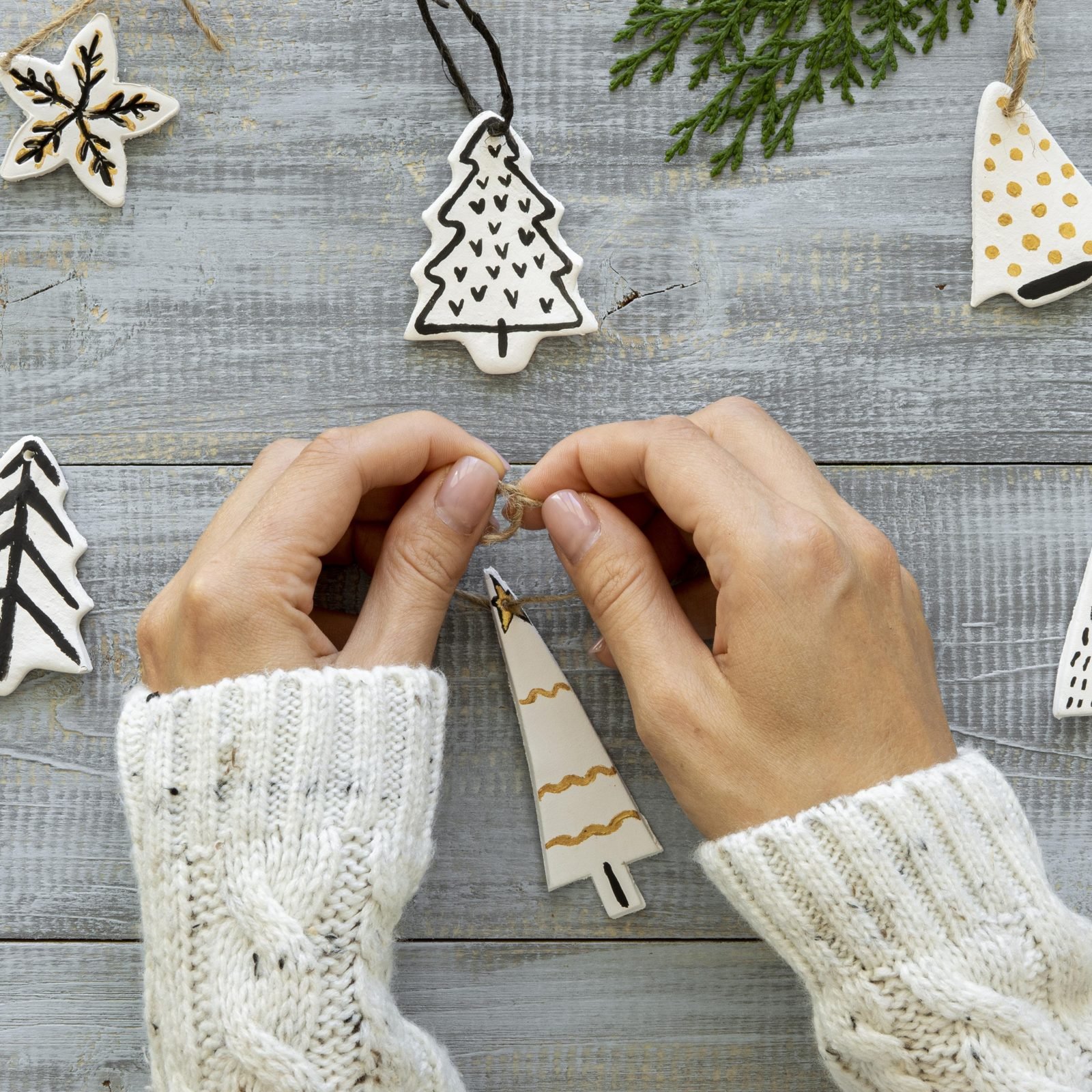 Hands tying twine onto handmade white Christmas ornaments shaped like trees and stars