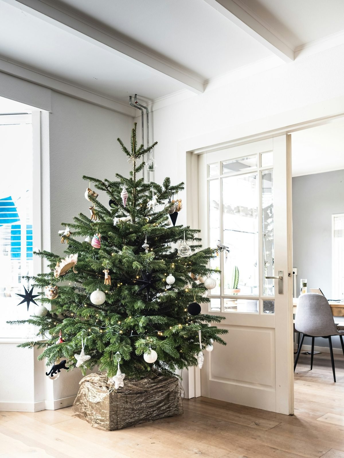 Árvore de Natal com bolas brancas e prateadas ao lado de uma porta de vidro em sala clara