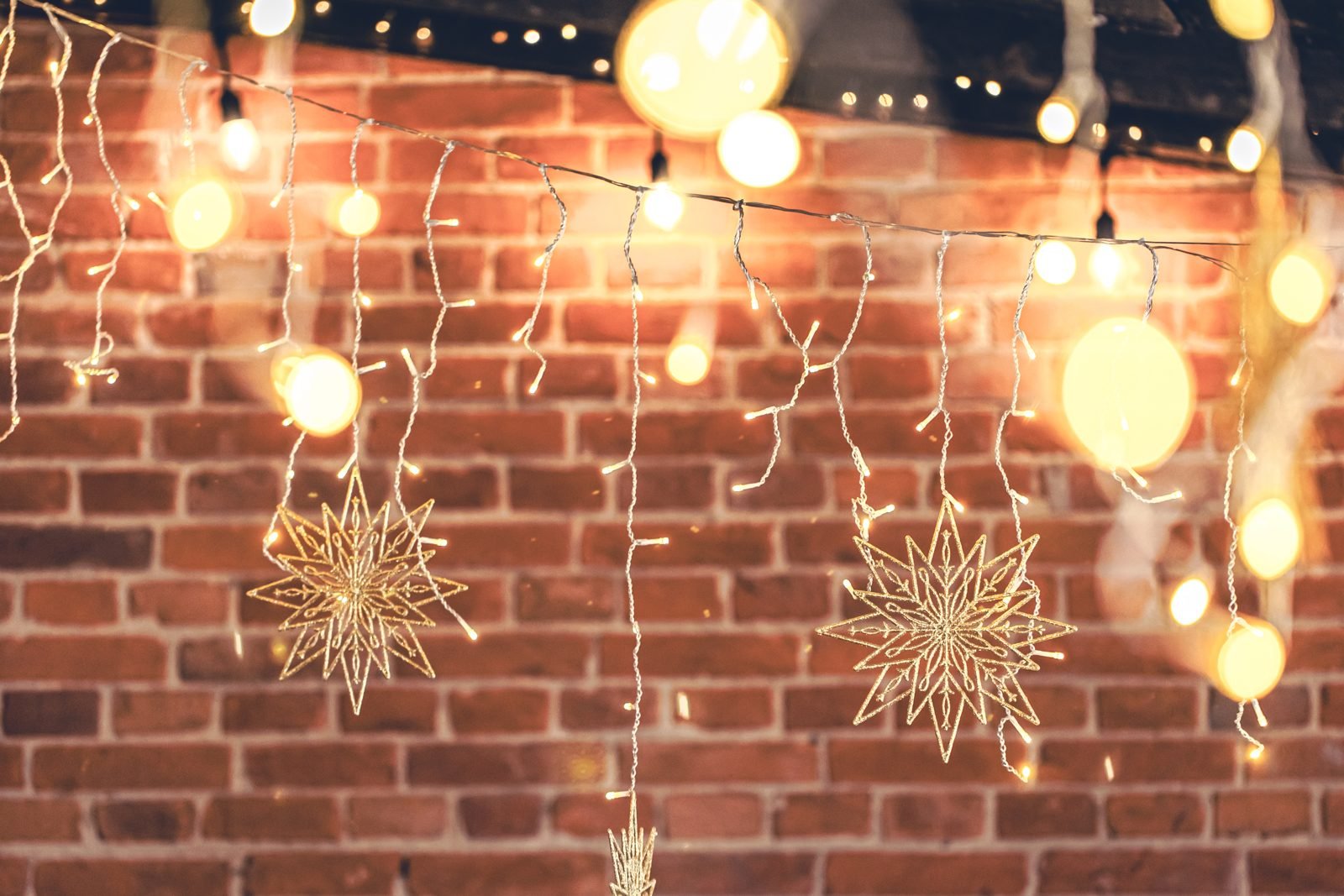 String lights and decorative stars hanging on a brick wall at night