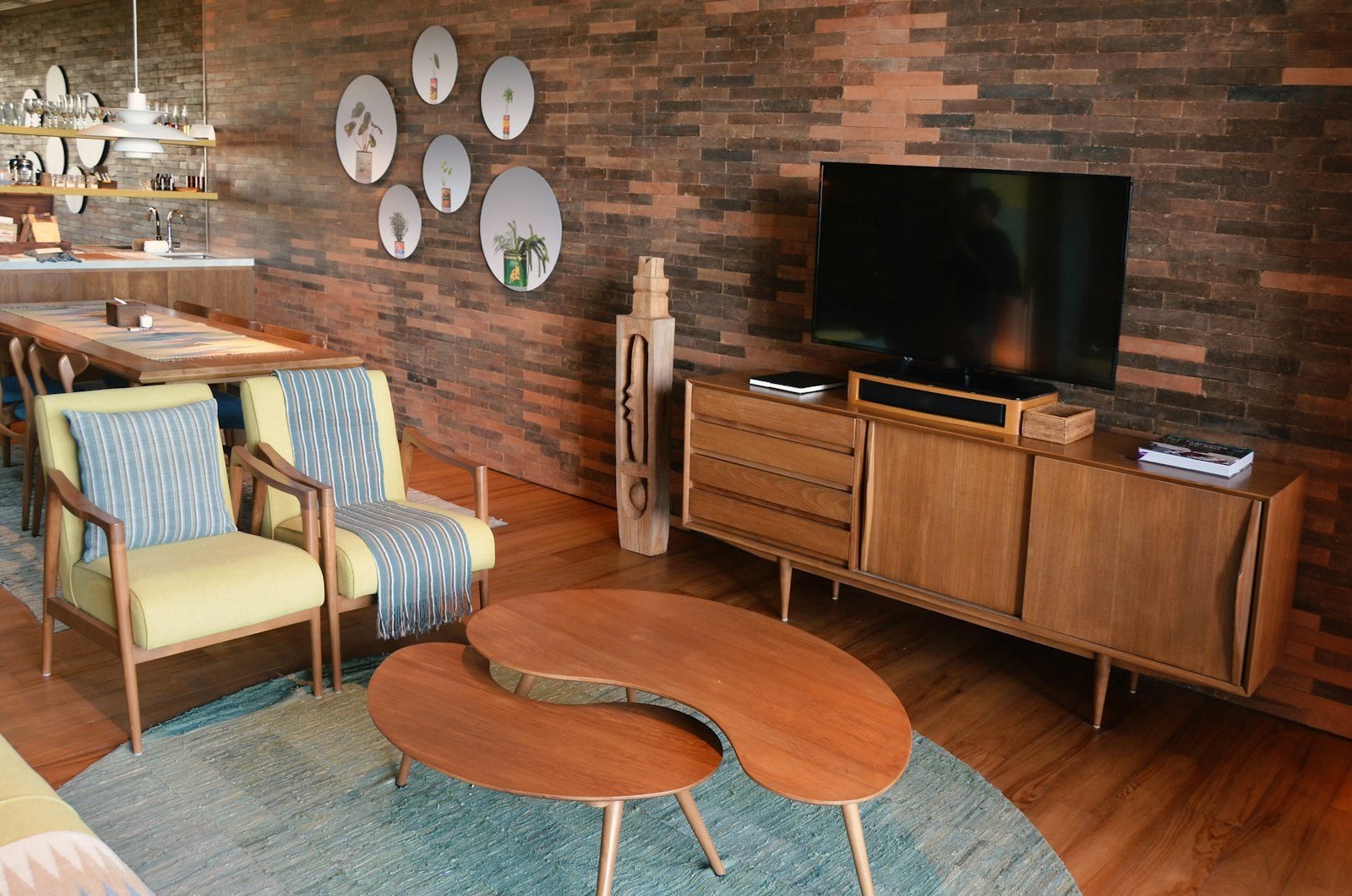Sala em estilo mid-century com poltronas de madeira amarelas, mesas de centro orgânicas, aparador baixo e parede de tijolinhos