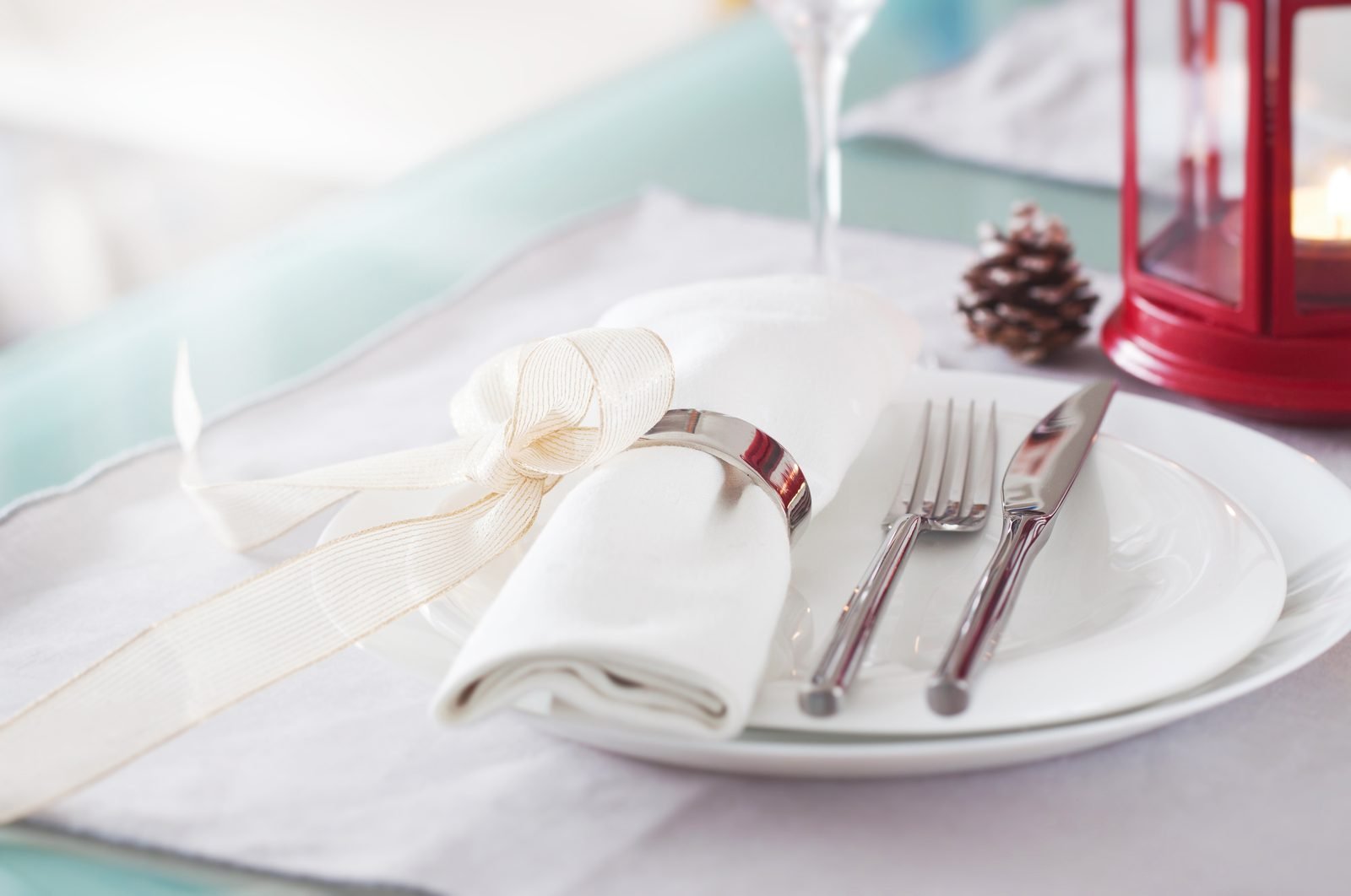 Christmas place setting with a white plate, cloth napkin in a silver ring, cutlery and a glass