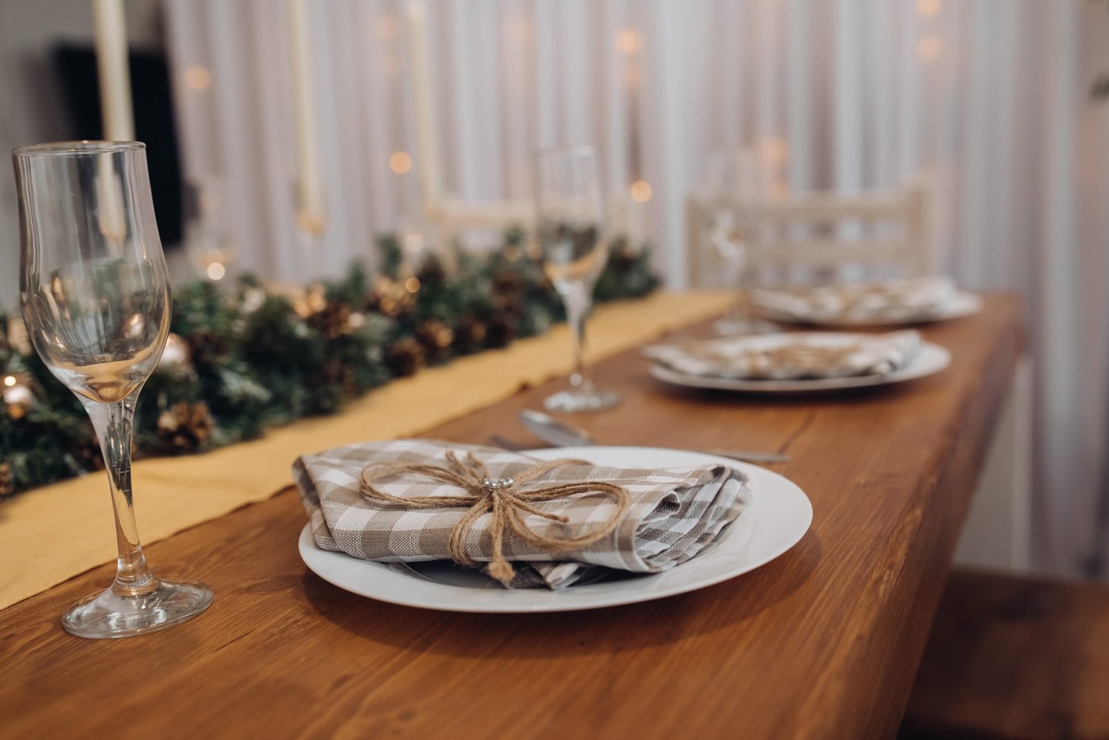 Wooden table with a pine garland down the center, plates with plaid napkins tied with twine and glasses