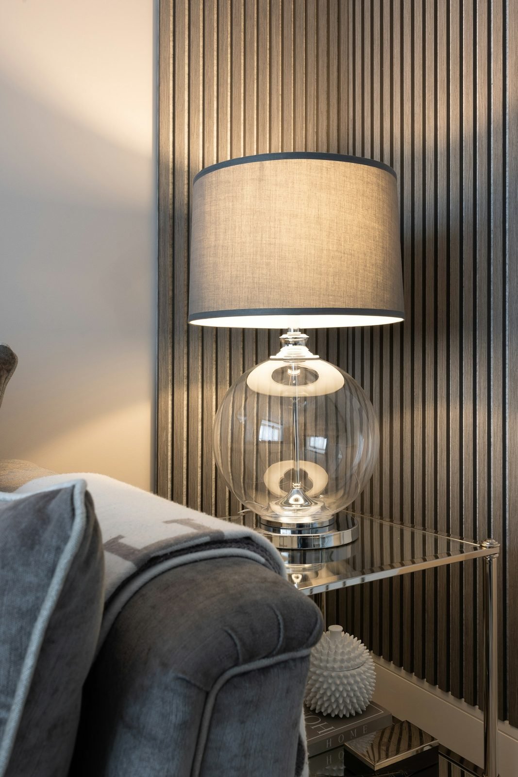Living room corner with a dark slatted textured wall, glass-based table lamp and gray sofa