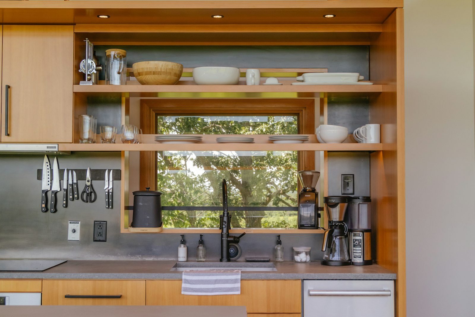 Kitchen with light wood cabinetry, open shelving and a gray backsplash behind the counter