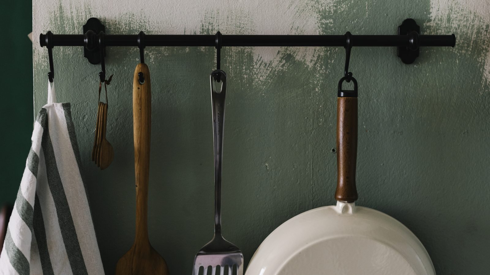 Kitchen utensils hanging from a black rail against a green wall