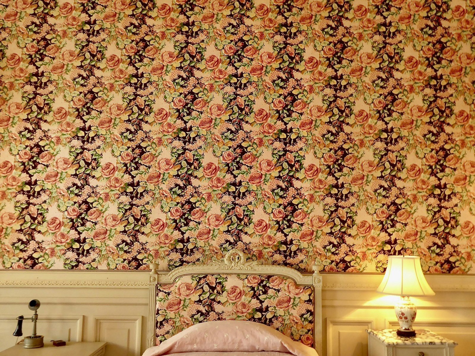Vintage-style bedroom with pink and burgundy floral wallpaper and a lit table lamp