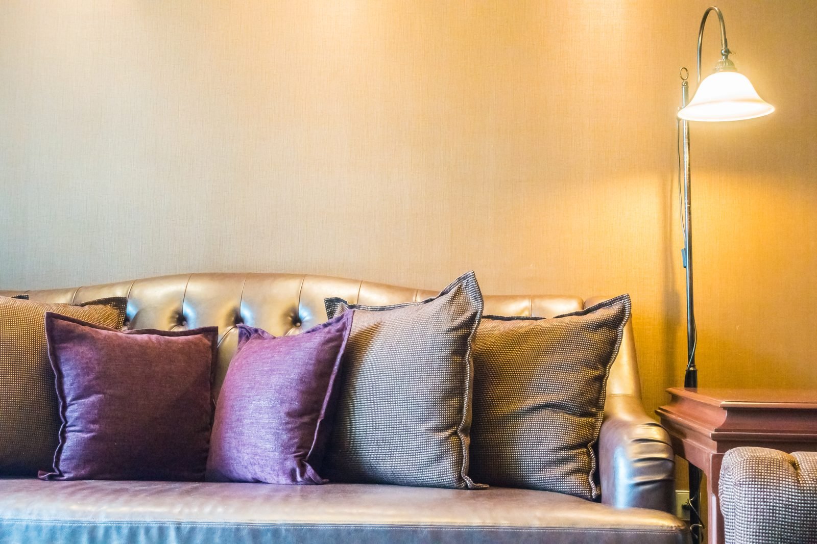 Leather sofa with purple and gray pillows next to a lit floor lamp and a wooden side table