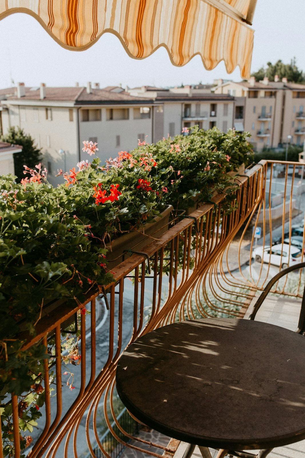 Varanda com floreiras floridas presas ao guarda-corpo, toldo listrado e mesa bistrô