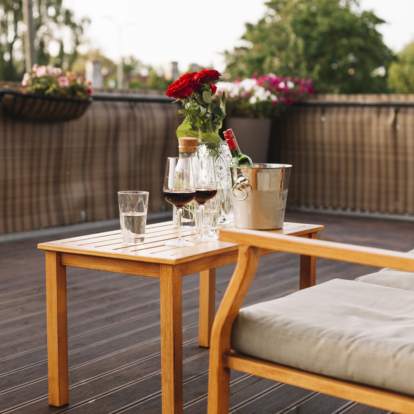 Mesa lateral de madeira com taças de vinho, balde de gelo e flores em varanda com deck
